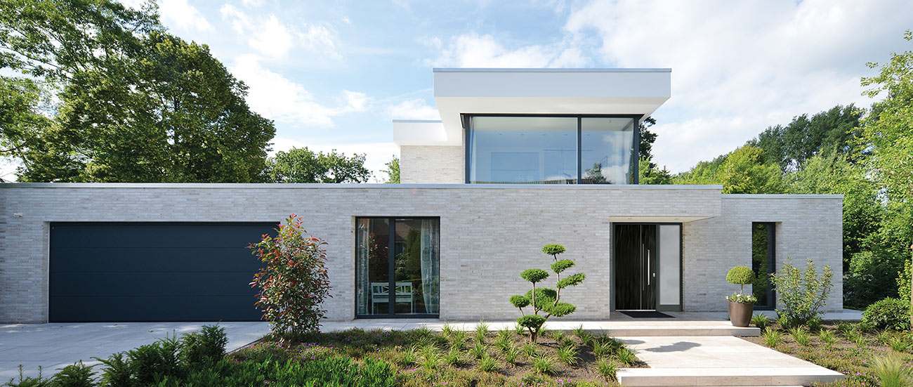 Modernes Block-Wohnhaus mit großen Fenstern, Garagentor und Haustür.