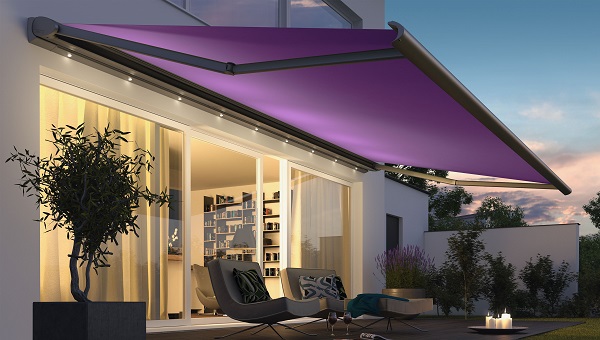 Die Terrassenmarkise Cassitta 2, violett, in der Abenddämmerung, mit Blick in das Wohnzimmer.